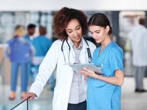 A picture of 2 female healthcare workers an an electronic device with a System C healthcare character in the background.