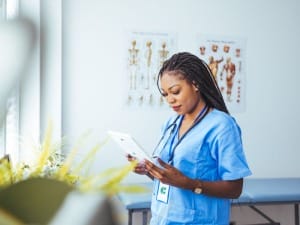A picture of a female healthcare worker in blue scrubs using CareFlow EPR (Electronic Patient Record) an an electronic device.