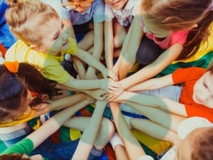 A picture of children putting their hands in the middle with a System C logo in the background.