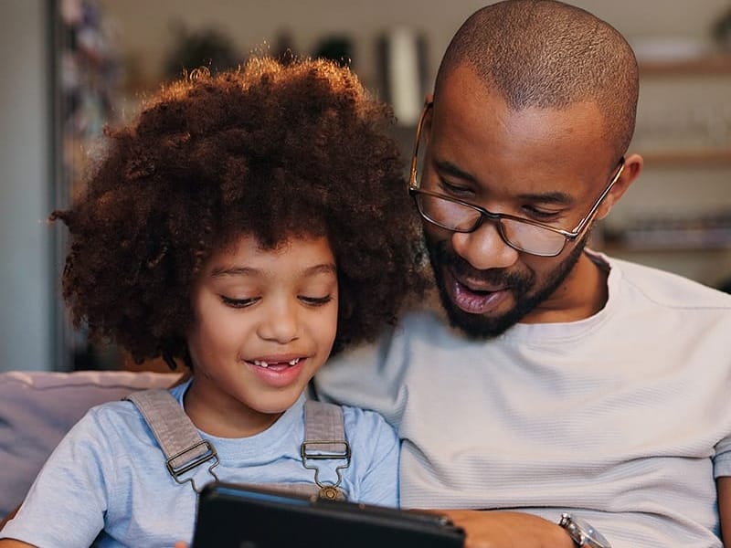 A picture of a parent with a young child looking at an electronic device and smiling.